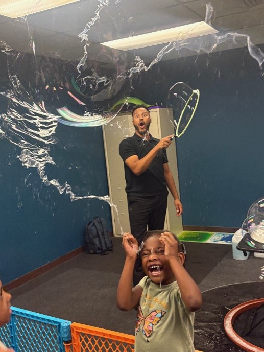 Bubbleologist Daniel Garcia makes bubbles while a Marcus Avenue student laughs.