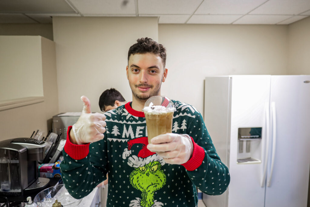 A BCCS student holds a cup of coffee he made and gives a thumbs up.