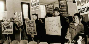 A group of people gathered in protest of Willowbrook. Signs read "Willowbrook, disgrace" and "Shame!"