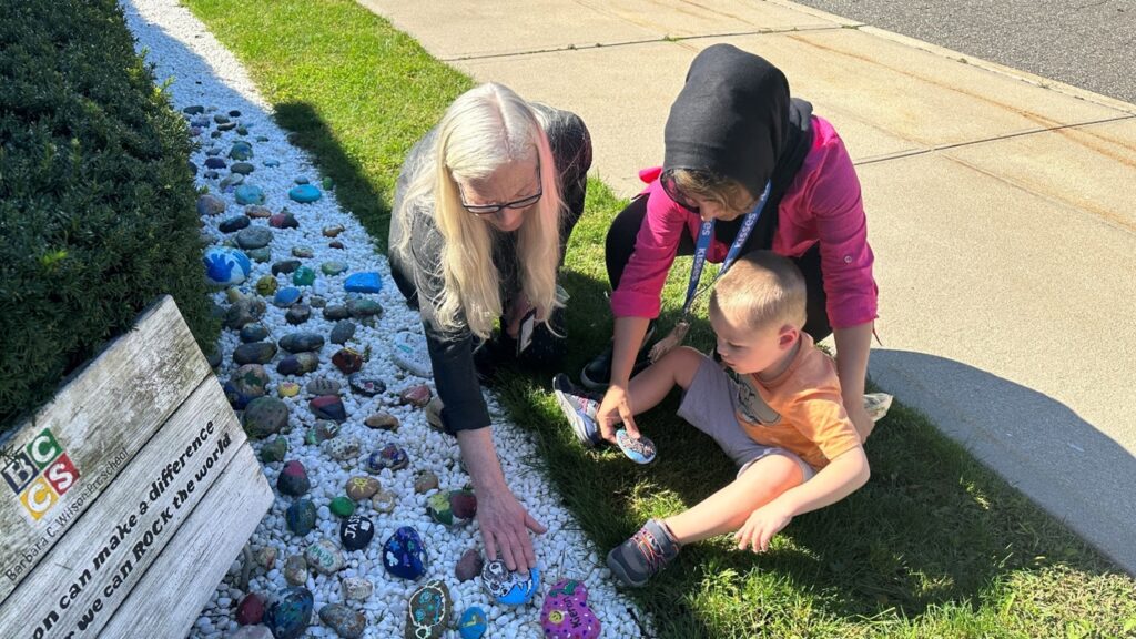 Teachers and a student add a stone to the DEI Rock Garden