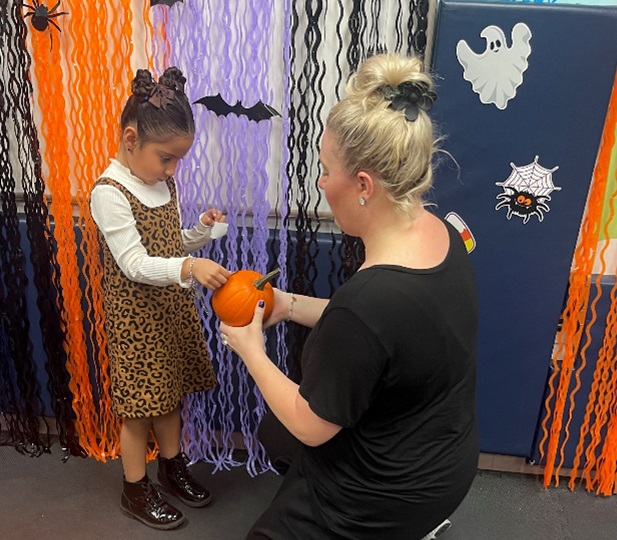 A Marcus Avenue School teacher helps a student decorate a pumpkin