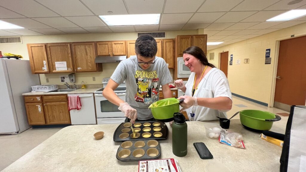 A student works on cooking skills with a staff member in the model apartment.