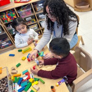 A teacher helps two BCCS students with blocks