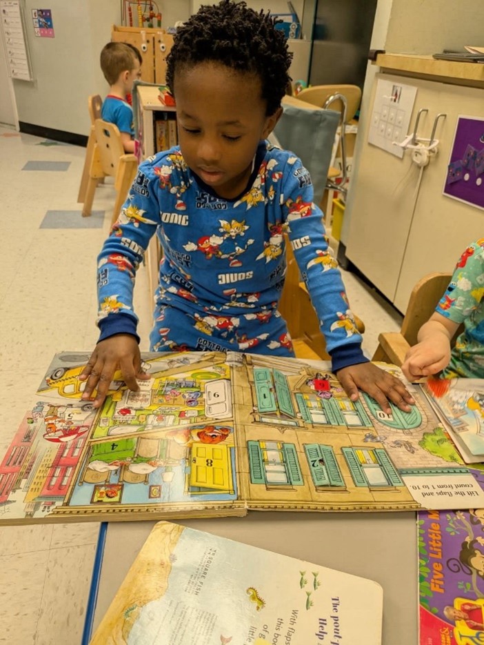 A Barbara C. Wilson Preschool student reads a book in his pajamas for Read Across America