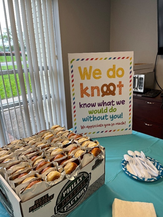 A sign reading "We do knot know what we would do without you! We appreciate you so much!" is on display with a box of pretzels.