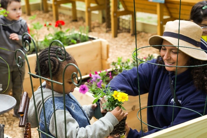 A BCCS teacher hands a student a yellow flower in the sensory garden.