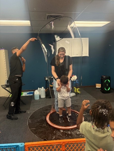 The bubbleologist creates a large bubble around a Marcus Avenue teacher and student.