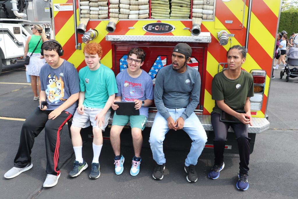 Five young men supported by the Children's Residential Program sit on the back of a firetruck at the touch-a-truck event.