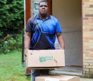 Transition Program student Judley Toussaint carries box labeled "Island Harvest."
