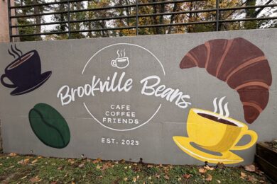 A painted wall reads "Brookville Beans Cafe Coffee Friends Est. 2025" with paintings of coffee cups, a croissant and a coffee bean.